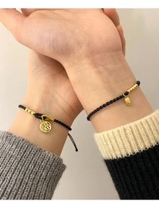 Detail of hand-woven black cord bracelets with gold Fu charms for couples on wrists