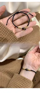 Detail of black woven cord bracelet with gold Fu charm and adjustable drawstring closure