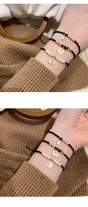 Detail of hand-woven black cord bracelet with gold Fu charm and white pearls on wrist