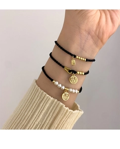Detailed view of woven bracelets with gold Fu charms and pearls on model wrist