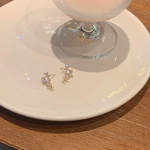 Detailed close-up of floral stud earrings with purple enamel and rhinestones on white ceramic