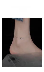 Detail of silver heart anklet with black inlay on model ankle against dark background
