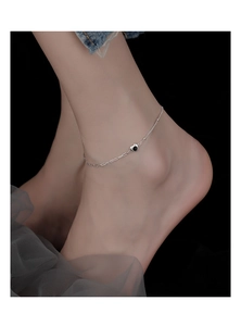 Close-up of minimalist silver anklet with black heart charm on ankle over dark mesh background