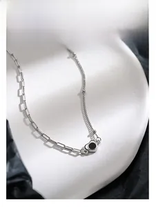 Detail showing asymmetric silver chain with a black heart pendant on a white tray