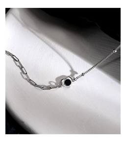 Detailed close-up of a silver heart anklet with black onyx inlay on a white texture