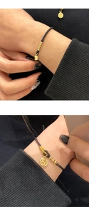 Close-up of black braided cord bracelet with gold beads and Fu character pendant