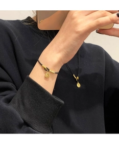 Close-up of golden Fu charm pendant and black woven cord bracelet set for couples