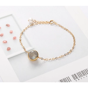 Macro detail of gold thin chain bracelet with translucent gemstone and pearl accent