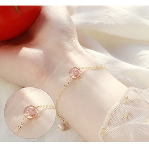 Macro shot of gold bracelet with strawberry quartz and a white pearl on a model