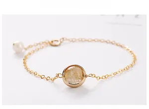 Detail of gold chain bracelet with round rutilated quartz and delicate pearl charm