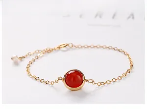 Close-up of a large red crystal bead on a delicate gold chain with a white pearl accent