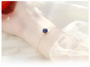 Close-up of a minimalist gold chain bracelet featuring a round blue lapis lazuli stone