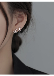 Close-up of minimalist silver hollow heart earrings worn on ear showing delicate metal texture