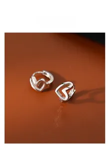 Macro shot of silver hollow heart-shaped huggie earrings on brown leather background