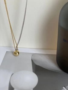 Detail of mixed-metal necklace with golden sphere pendant and asymmetrical chain links