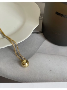 Detailed macro view of dual-tone gold bead chain and polished gold sphere pendant