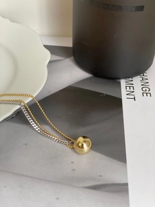 Detail view of a two-tone chain necklace with a polished gold ball pendant on a white plate