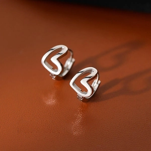 Polished silver heart-shaped hollow hoop earrings on a textured leather background