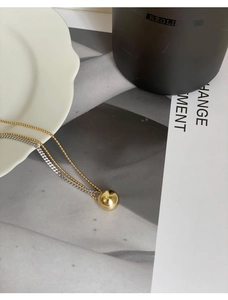 Detail of minimalist mixed metal necklace featuring a gold ball pendant and layered chains