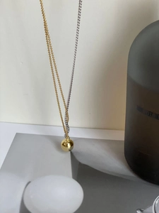 Detail of mixed-metal necklace with golden sphere pendant and bi-color chain