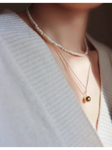 Detail of layered necklace featuring shell square beads and golden sphere pendant