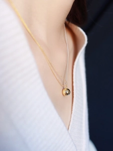 Close-up of minimalist gold bead pendant necklace worn over a white ribbed knit sweater
