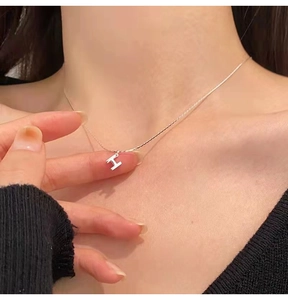 Gros plan d'un collier pendentif lettre H argenté minimaliste sur le mannequin