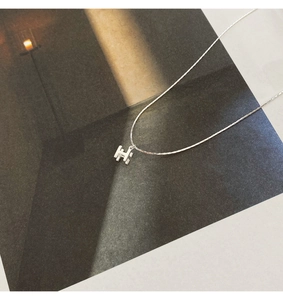 Gros plan du collier avec pendentif H argenté minimaliste sur fond esthétique