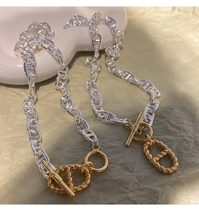 Gros plan d'un collier à maillons mixtes avec fermoir en T doré sur une assiette blanche