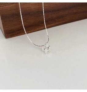 Gros plan du pendentif lettre H en argent avec chaîne fine sur un bloc en bois
