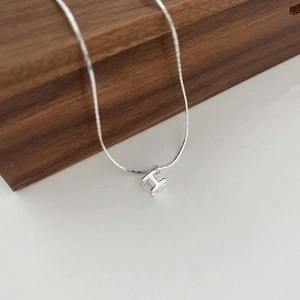 Gros plan du collier avec pendentif lettre H argenté minimaliste au fini métallique poli