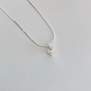 Gros plan du collier avec pendentif lettre H argenté et texture de chaîne en métal