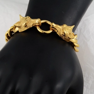 Détail d'un bracelet gourmette doré avec deux têtes de loup sur un support d'exposition noir