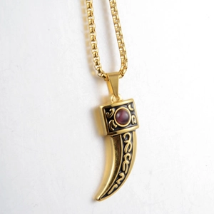 Macro detail of gold wolf tooth pendant with black enamel patterns and red gemstone