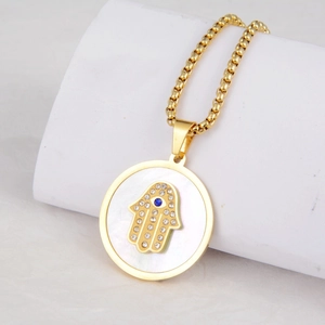 Macro detail of gold Hamsa hand pendant necklace with mother of pearl and blue stone