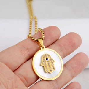 Close-up of golden Hamsa Hand pendant with mother of pearl inlay and blue gemstone