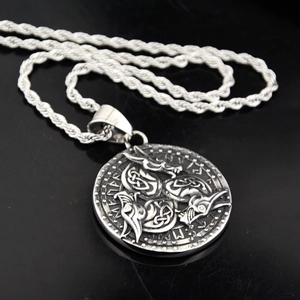 Macro detail of Viking raven pendant with runes and silver twist chain on black surface