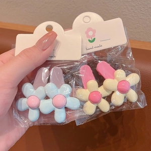 Detail of four handmade macaron flower hair clips on white card packaging with duckbill clips