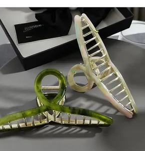 Detail of oversized marble acetate hair claws in green and cream with golden metal teeth
