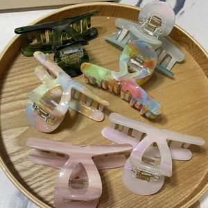 Detailed overhead view of six colorful matte and marble hair claws on a round wooden tray