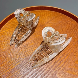 Close-up of two white marble acetate hair claws on a circular wooden tray with metal springs