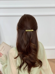 Detailed view of five pale green jelly beads on a gold metal hair clip worn by a model