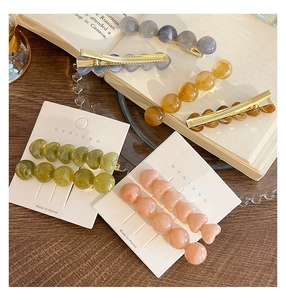 Close-up of heart and bead resin hair clips in pastel colors on a gold duckbill clip