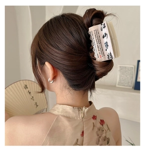 Macro detail of cream hair claw with black calligraphy and red seal on elegant updo hair