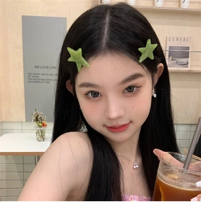 Detail of two matte green star-shaped hair clips worn by a model in a cozy cafe setting