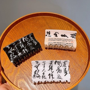 Three Chinese ink calligraphy hair claw clips in black, white, and beige on a wooden tray