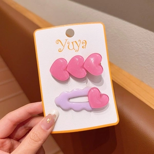 Dettaglio di fermagli per capelli con cuori rosa e forcina ondulata viola su carta