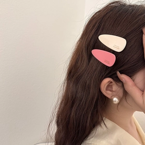 Gros plan de barrettes goutte en acétate crème et corail sur cheveux châtain foncé