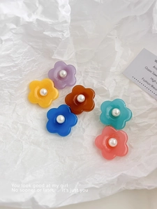 Détail de six barrettes à fleurs colorées en résine avec perles sur fond blanc texturé