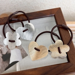 Detailed macro view of brushed metal heart and flower charms on brown hair ties
